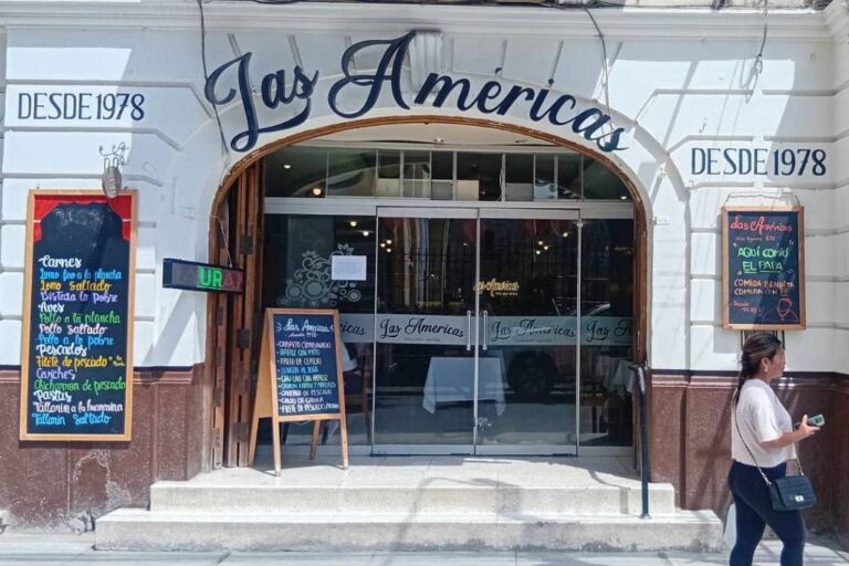 A imagem mostra a fachada do restaurante Las Américas, que está localizada em um edifício de estilo arquitetônico clássico. A entrada é ampla, com portas de vidro e uma placa com o nome